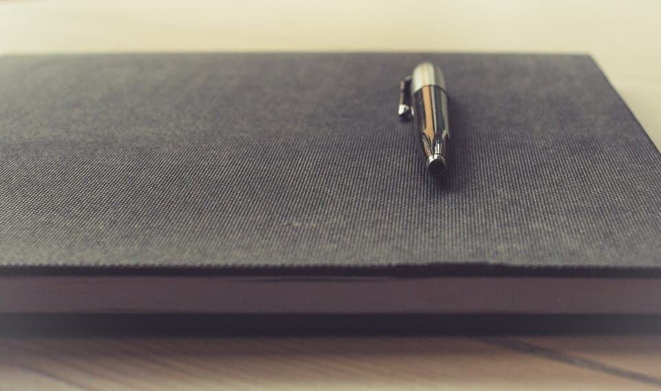 A pen resting on a closed notebook in soft light (illustrative)