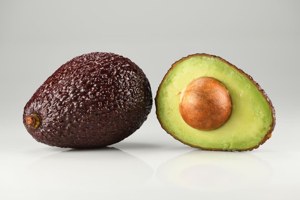 A whole avocado next to a halved avocado with its stone (illustrative)