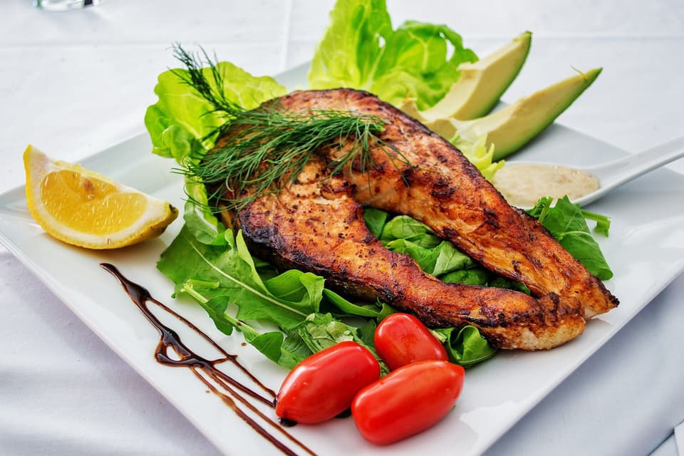 Grilled salmon on green leaves with avocado, tomatoes and lemon (illustrative)