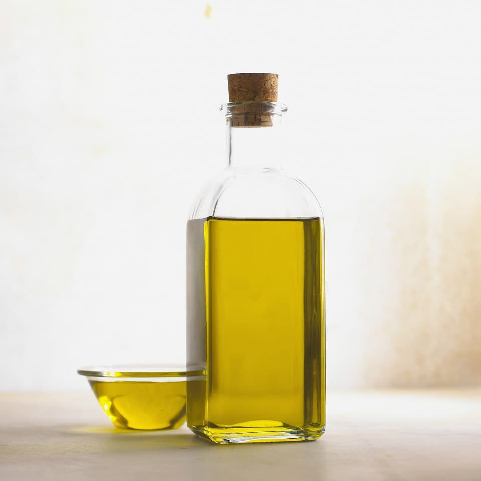A glass bottle of golden olive oil with a cork stopper (illustrative)