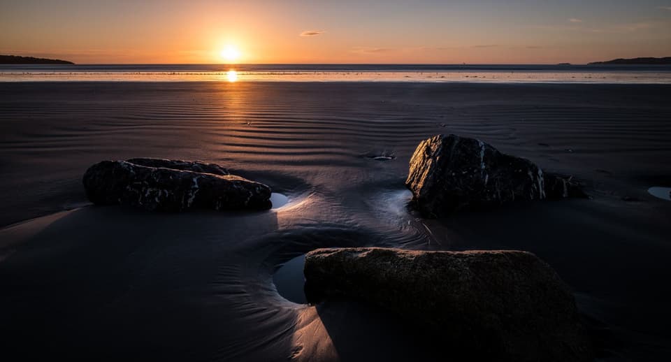 Sunrise over wet sand and rocks on a quiet beach at low tide (illustrative)