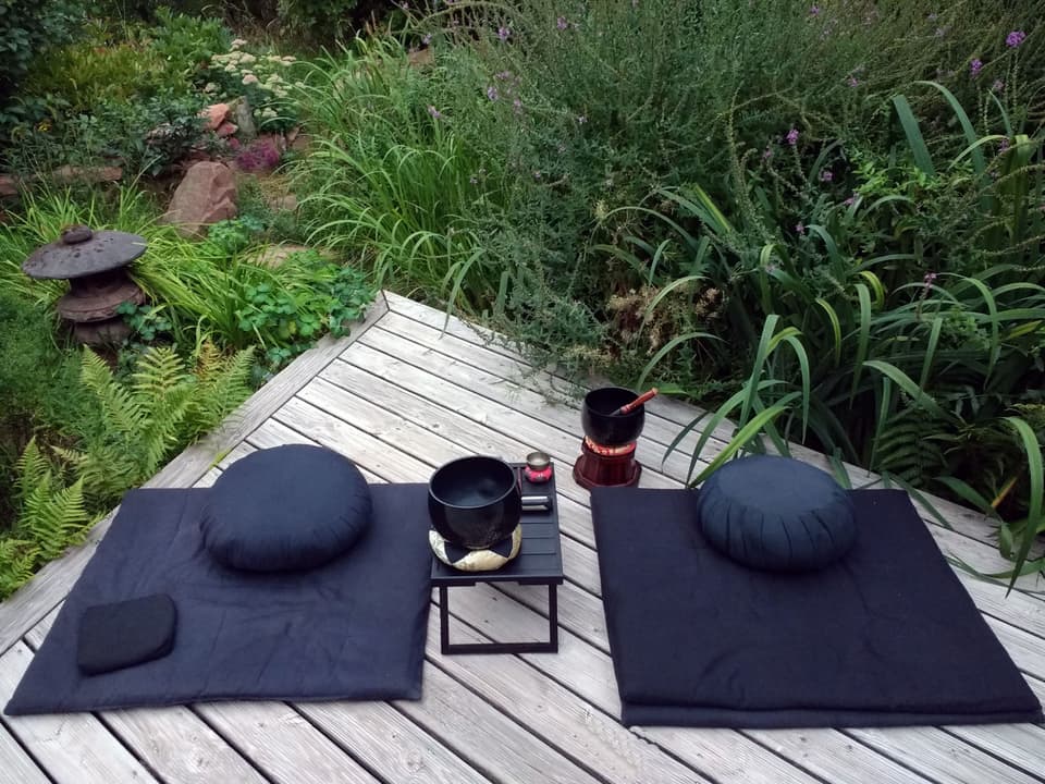 Two meditation cushions and a singing bowl on a wooden deck in a garden (illustrative)