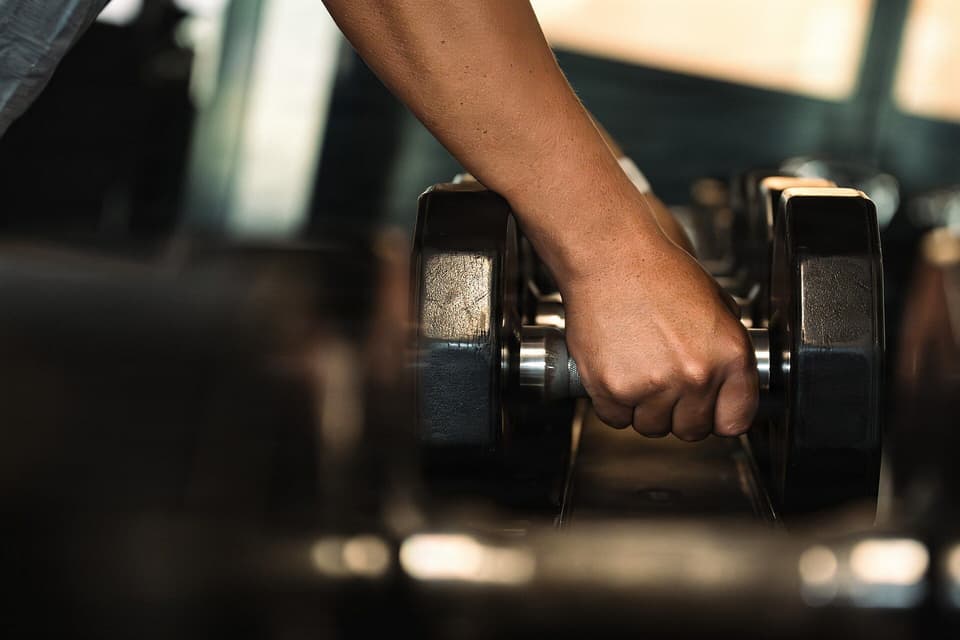 A hand lifting a dumbbell from a gym rack, close-up (illustrative)
